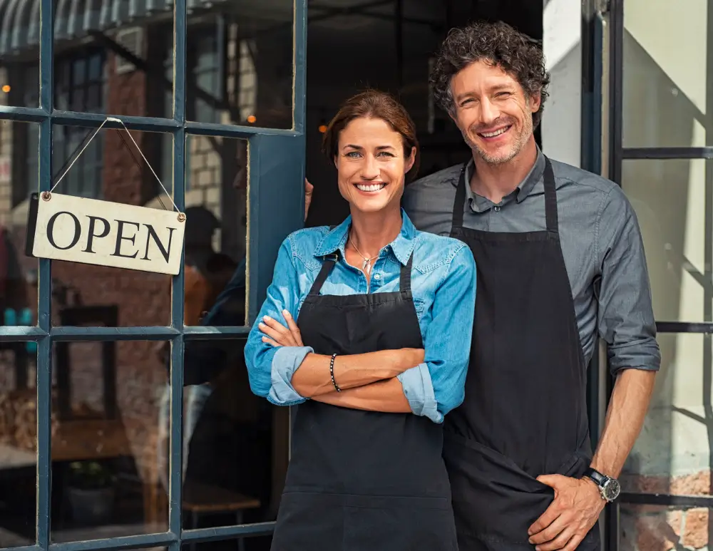 A man and a woman in front of their store next to an open sign