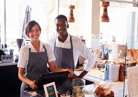 A man and woman in aprons behind the counter of a cafe